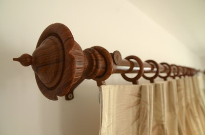 A close-up of pinch-pleat drapes hooked to a rings on a wooden bohemian style curtain rod.
