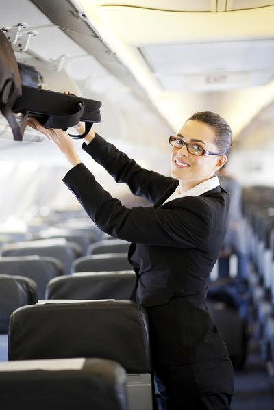 A woman on an airplane stores her carry-on luggage in an overhead bin.
