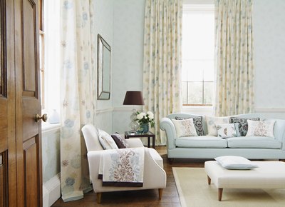 Curtains gracing ceiling to floor windows in a traditional living room decorated with soft patterns and hues.