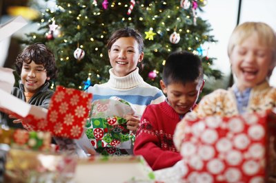 Four happy children open gifts by a decorated tree.