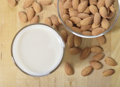 A small cup of almond milk, next to a bowl of raw almond nuts.