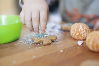 A close-up of a child adding sprinkles to a gingerbread cookie.