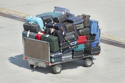 Checked bags are stacked onto a luggage cart in an airport terminal lot.