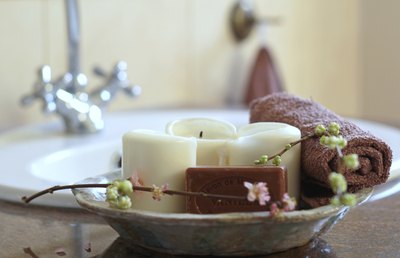 A close-up of a bowl filled with candles, soap, a rolled washcloth, and a sprig of flowering vine.