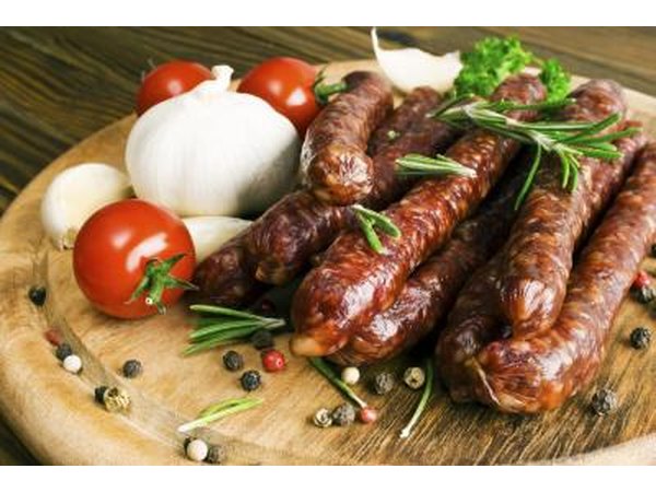 Pork sausages on a cutting board with onions and tomatoes.