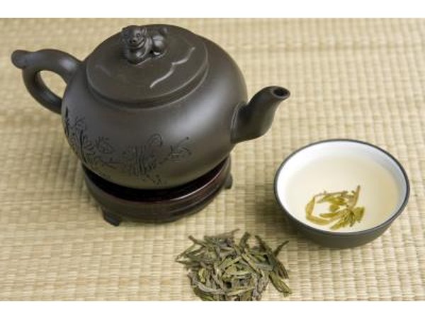 A teapot, cup of green tea, and tea leaves on a bamboo mat