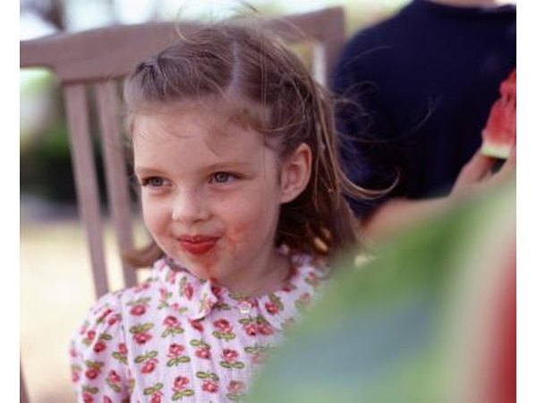 A little girl has red fruit on her chin.