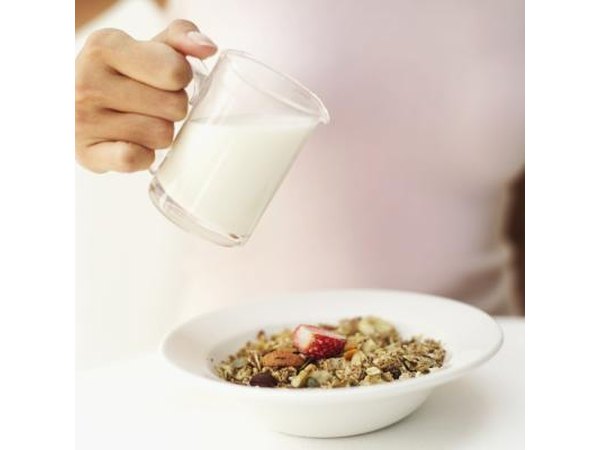 A woman pours skim milk over cereal.