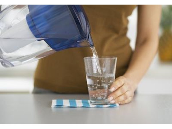 A woman pouring a glass of filtered water from a pitcher a the kitchen counter.