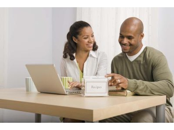 Couple looking at cookbook and laptop