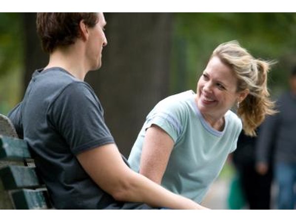 A couple smiles and converses on a park bench.