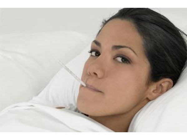 Young woman in bed with thermometer in mouth.