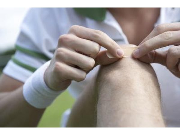 A tennis player adheres a bandage to his knee.