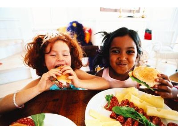 Two girls eat finger sandwiches.