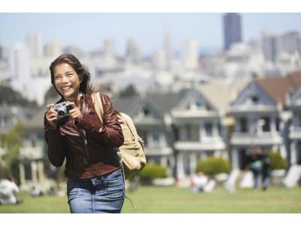 A woman with a camera walks through a neighborhood with Victorian homes.