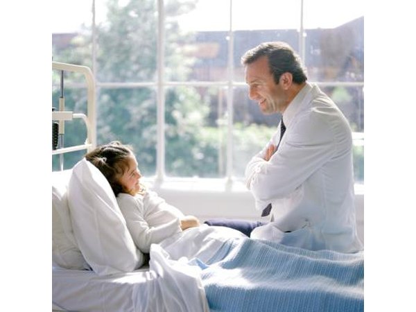 Doctor talking to female child in hospital bed.