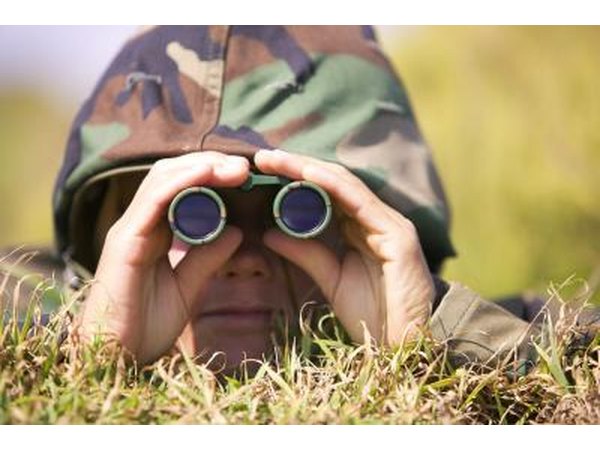 A soldier is laying in the field wearing camouflage.