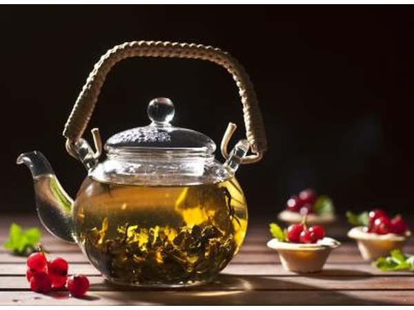 A teaport filled with green tea on a wooden table with garnishes