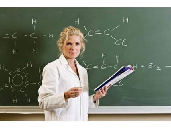 Female teacher holding book standing in front of blackboard.
