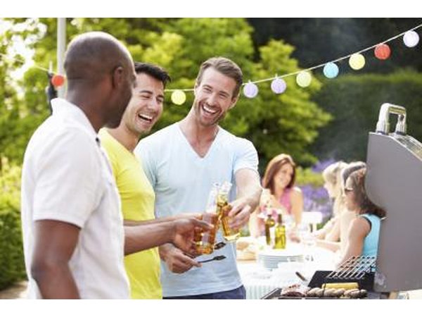 A group of men laugh and joke with one another while cooking at the barbecue