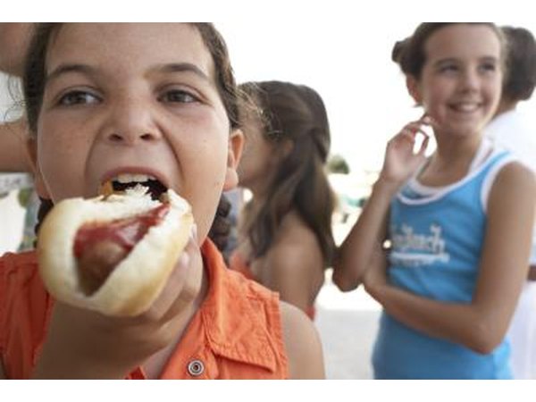A girl takes a bite of a hot dog with ketchup.