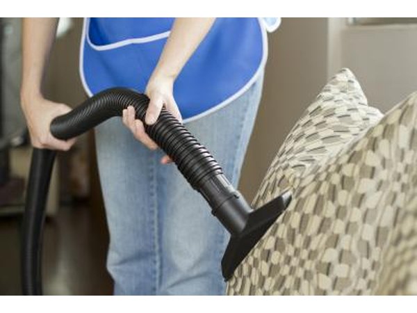 A woman uses an upholstery attachment to vaccum a couch.