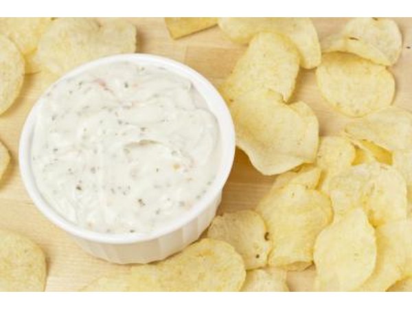 Potato chips around a bowl of french onion dip on a cutting board.