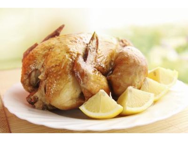 A roasted chicken on a platter with fresh lemon wedges.