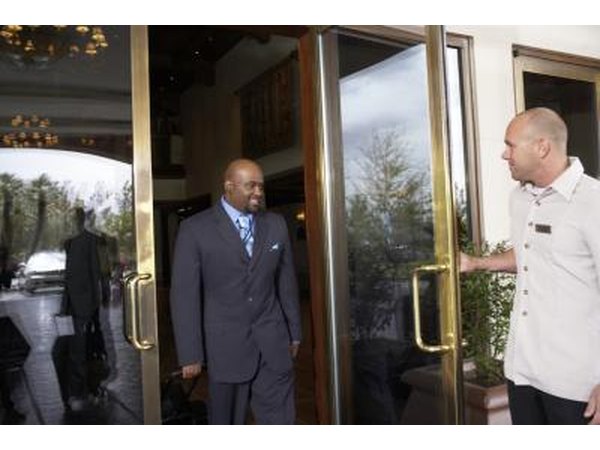 A hotel employee opens the door for a smiling guest.