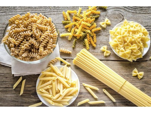An assortment of dried pastas on a wooden countertop.