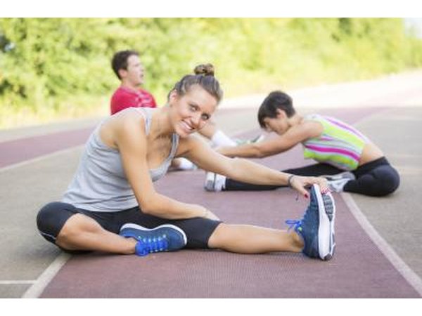 Three athletes stretch on a track.