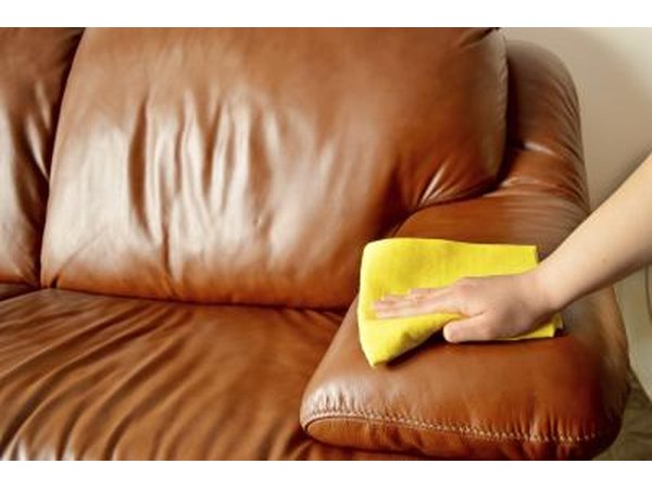 A woman wipes a leather sofa with a soft cloth.