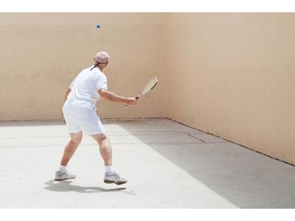 A senior hits a ball to the wall on an outdoor racquetball court.
