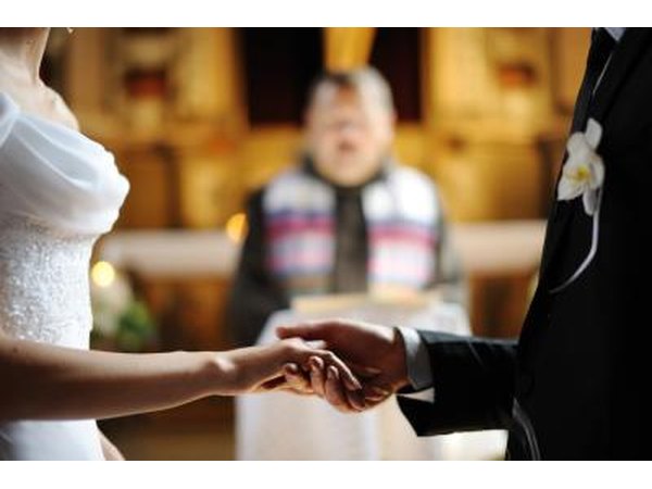 A groom holds his bride's hand during a wedding ceremony.