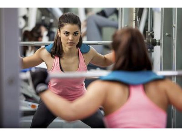 A young woman does barbell squats at the gym.
