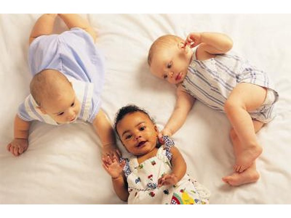 3 infants lay on a blanket together.