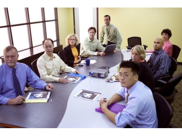 Employees sit at a curved table that divides into two in a conference room.