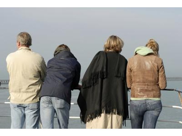 The backs of four cruise ship passengers looking over a rail.