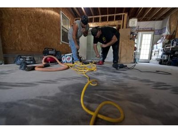 Men anchor a safe room below a car garage