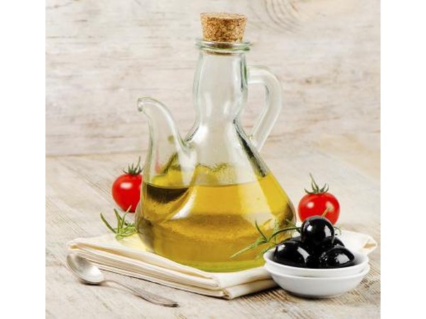 A bottle of olive oil with a some black olives and tomatoes