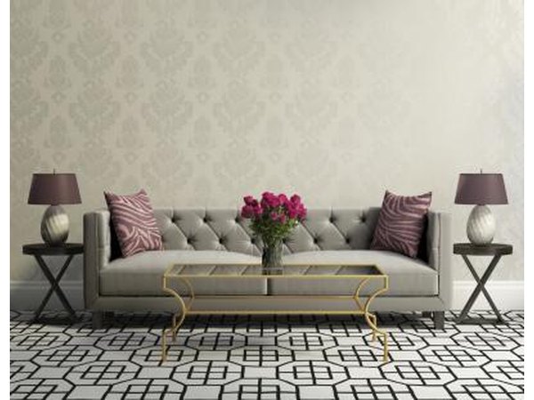 A vintage grey plush couch sits in between two matching classic wooden tables just wide enough to hold matching lamps.