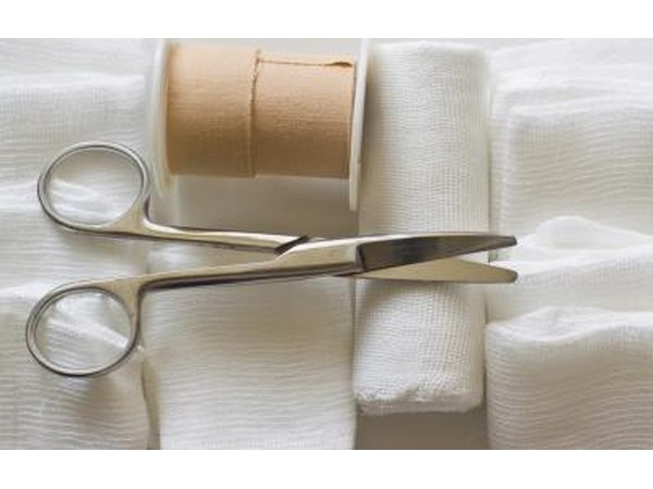 A pair of scissors and medical tape lay on top of rolls of clean gauze.
