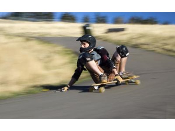A skater wearing a helmet and pads carves around a corner on a longboard.