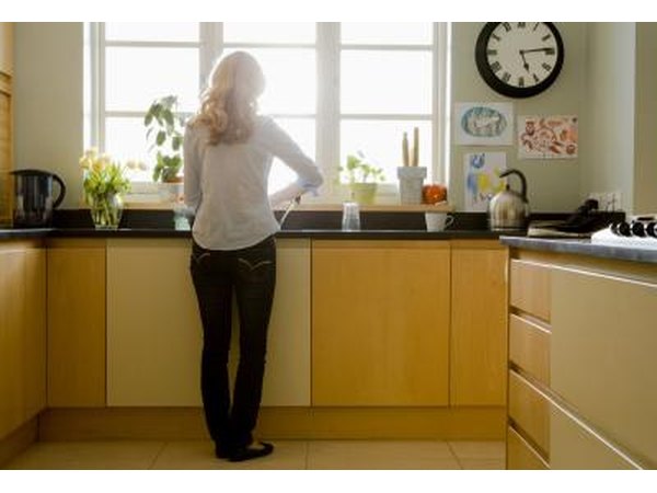 A woman stands at the sink in a kitchen.