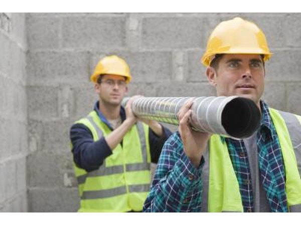 Two construction workers carrying pipe