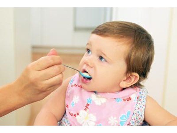 Toddler being spoon fed in high chair.