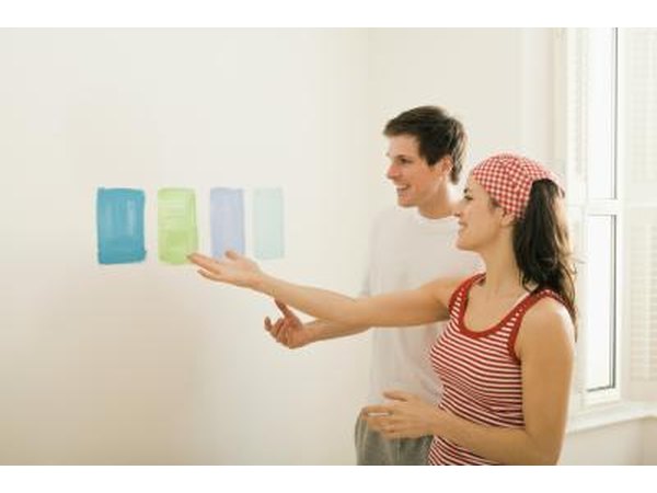 A couple compares paint samples on a white wall.