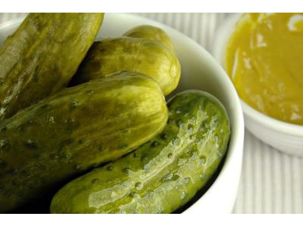 A close up of a small bowl of pickles next to a side of mustard