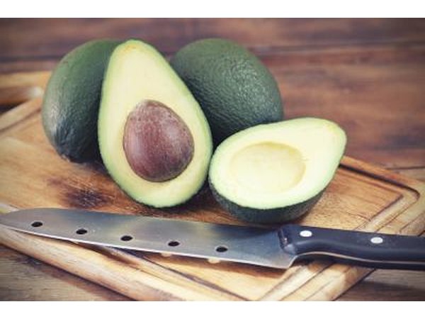 Halved avocados on a cutting board next to a knife.