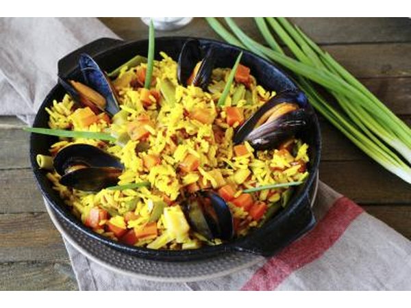 A pot of paella on a linen napkin on a wood table next to fresh scallions.